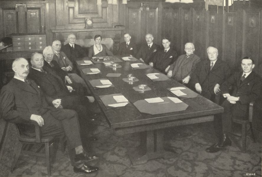 Photo of large table of men and one woman in the middle at head of table