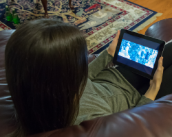 A person is lying on a couch watching a movie on a tablet.