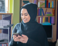 A person wearing a headscarf is smiling while looking at their phone in a library branch.