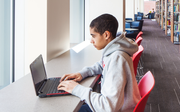 A teen looking at a laptop in the library